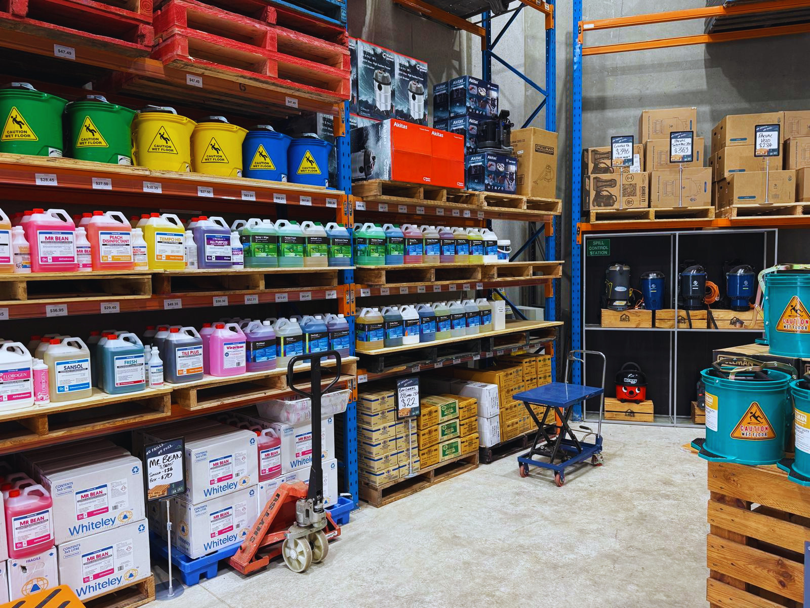 Warehouse interior with shelves stocked with various containers and boxes including Actichem, Whitely, Pacvac, Henry and Edco
