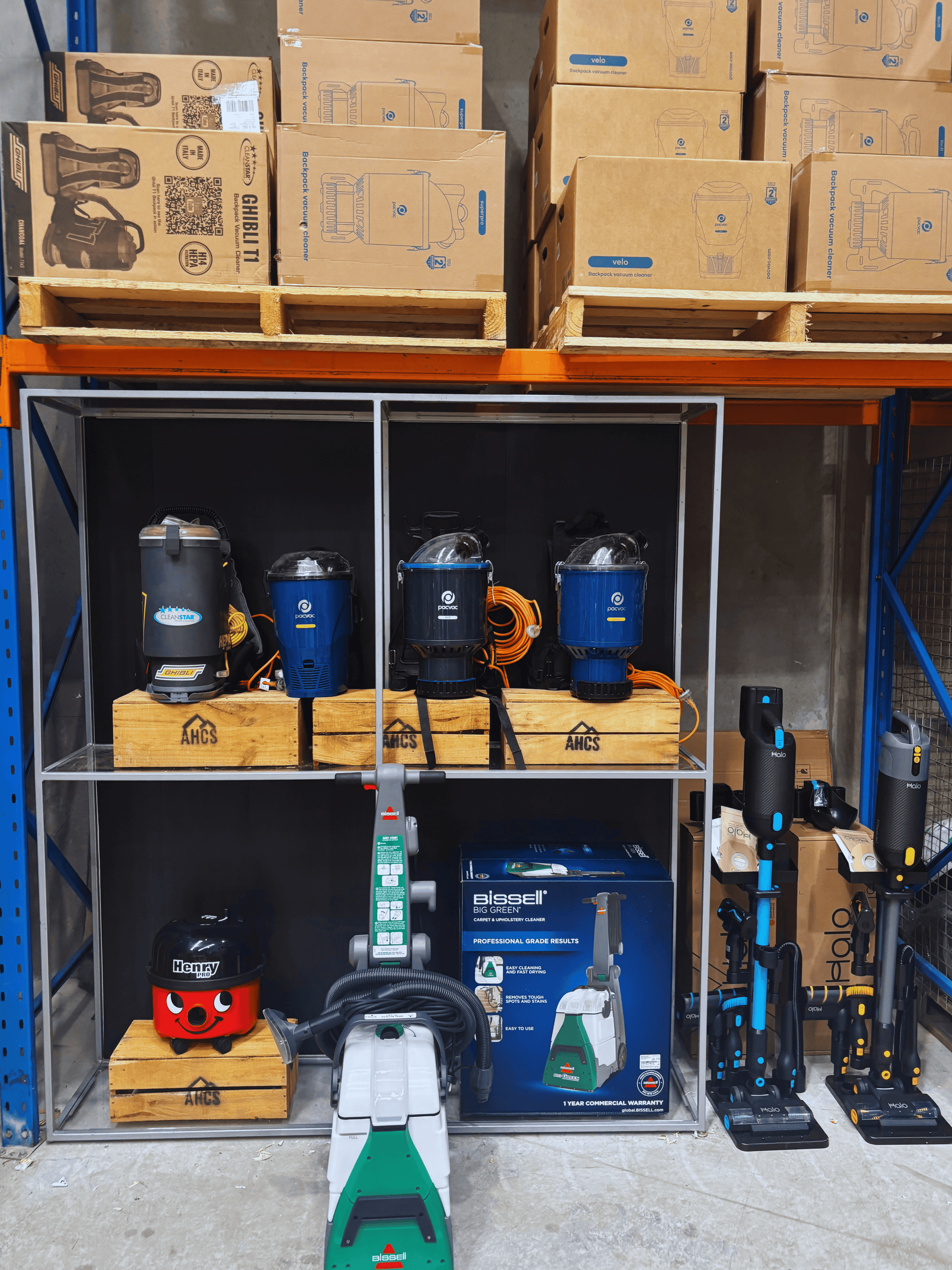 Shelving with commercial vacuum cleaners on shelves and stacked vacuum boxes above including Bissell Big Green, Numatic Henry, Pacvac Thrift, Pacvac Velo, Pacvac Superpro 700, Ghibli T1